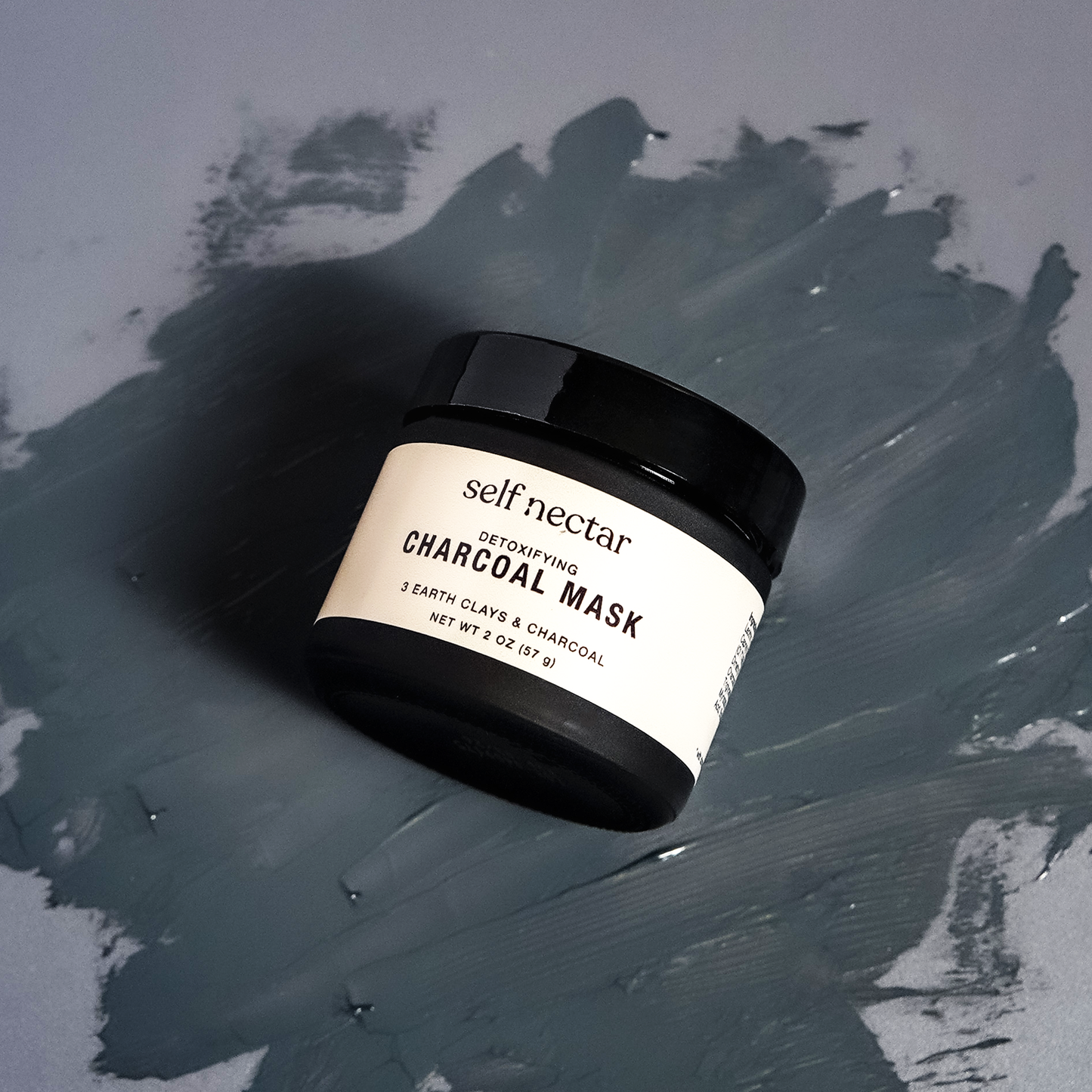 he top view of a detoxifying charcoal mask placed on a charcoal swatch, set against a charcoal background. The composition emphasizes the deep, rich tones and textures, reflecting the purifying properties of the charcoal mask for an invigorating skincare