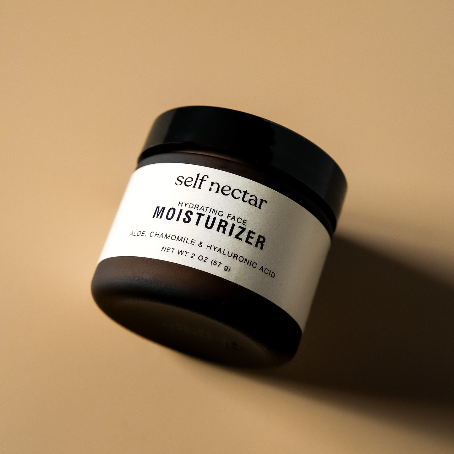 A flat lay view of a hydrating face moisturizer in an amber container, strategically placed on a neutral-colored surface. The product is labeled as a hydrating face moisturizer, and the composition features hard shadows, creating a visually striking prese