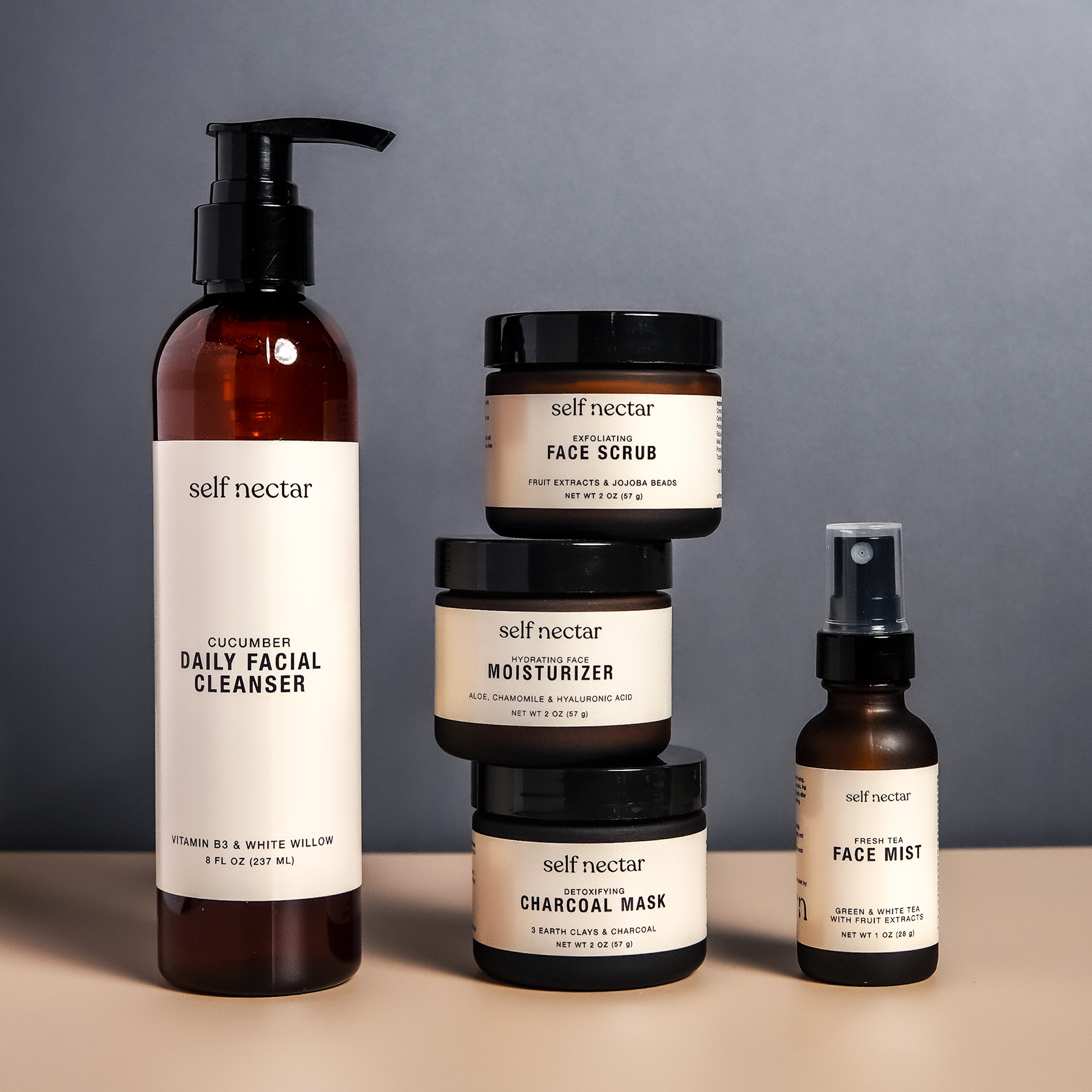 A captivating ensemble of skincare essentials, including a detoxifying charcoal mask, exfoliating face scrub, hydrating face moisturizer, fresh tea face mist, and cucumber daily facial cleanser. Set against a rich charcoal background, the dark tones enhan