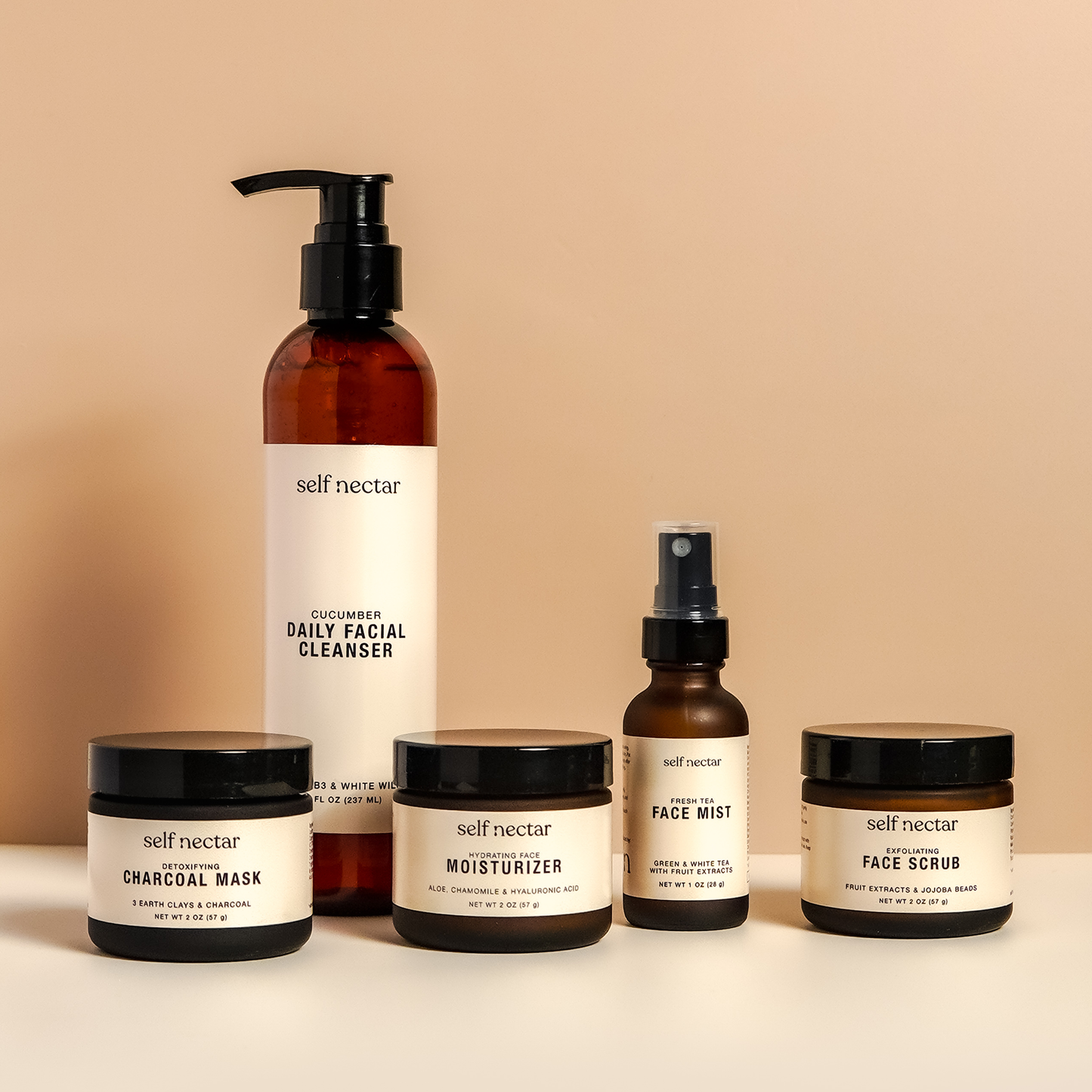 A curated collection of skincare essentials featuring a detoxifying charcoal mask, exfoliating face scrub, hydrating face moisturizer, fresh tea face mist, and cucumber daily facial cleanser. Arranged artfully on a neutral surface, the products create a h