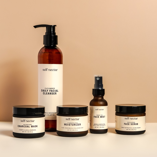 A curated collection of skincare essentials featuring a detoxifying charcoal mask, exfoliating face scrub, hydrating face moisturizer, fresh tea face mist, and cucumber daily facial cleanser. Arranged artfully on a neutral surface, the products create a h