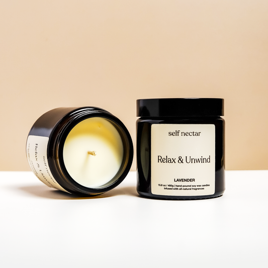 A soothing relax & unwind candle in a calming container on a neutral-colored surface. The product is labeled as a relax & unwind candle, presenting a clean and minimalist design to create a tranquil atmosphere.