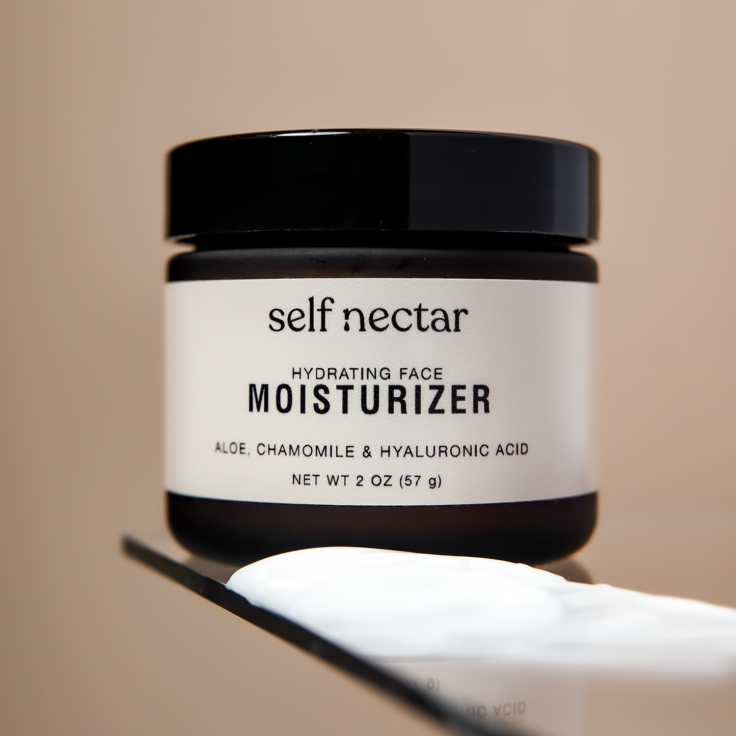 A hydrating face moisturizer in an amber container positioned on a glass surface, accompanied by a cream swatch in the foreground. The product is labeled as a hydrating face moisturizer, featuring a clean and minimalist skincare design.